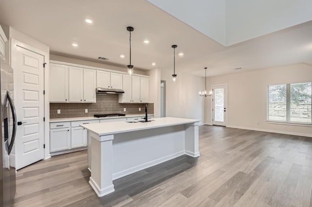 kitchen with hanging light fixtures, backsplash, sink, white cabinetry, and a kitchen island with sink