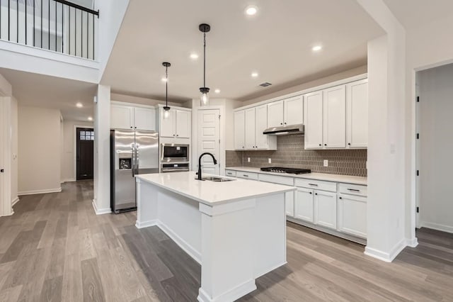 kitchen with appliances with stainless steel finishes, a center island with sink, white cabinets, decorative light fixtures, and sink