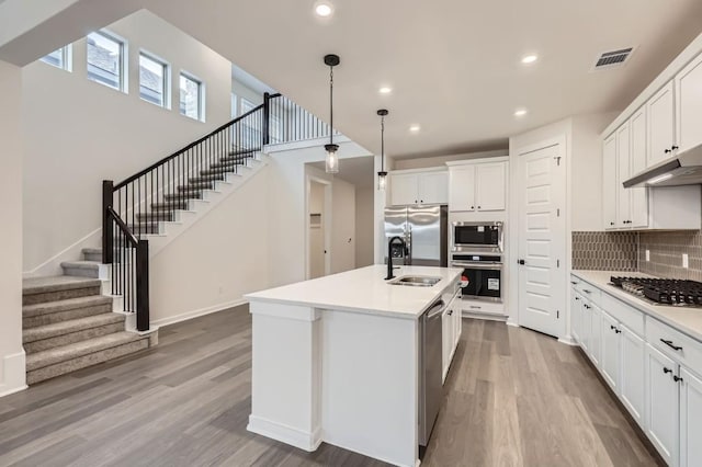 kitchen with an island with sink, white cabinetry, hanging light fixtures, sink, and appliances with stainless steel finishes