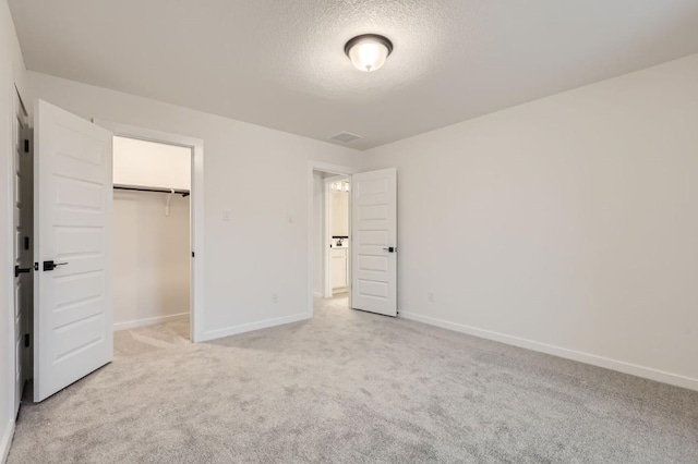 unfurnished bedroom featuring a textured ceiling, light carpet, a walk in closet, and a closet