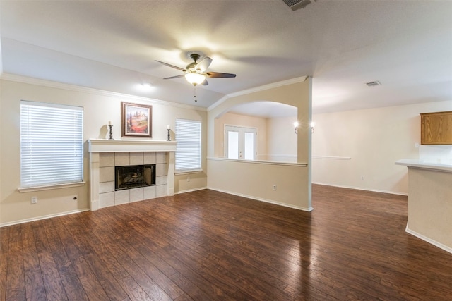 unfurnished living room featuring dark wood-type flooring, crown molding, a tile fireplace, and ceiling fan