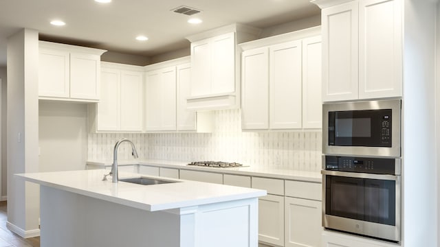 kitchen featuring sink, stainless steel appliances, tasteful backsplash, an island with sink, and white cabinets