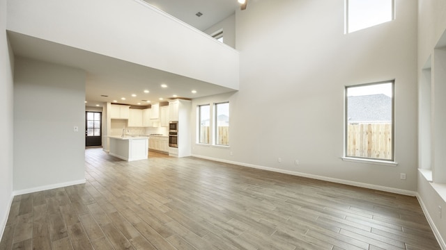 unfurnished living room with plenty of natural light, light hardwood / wood-style floors, sink, and a high ceiling