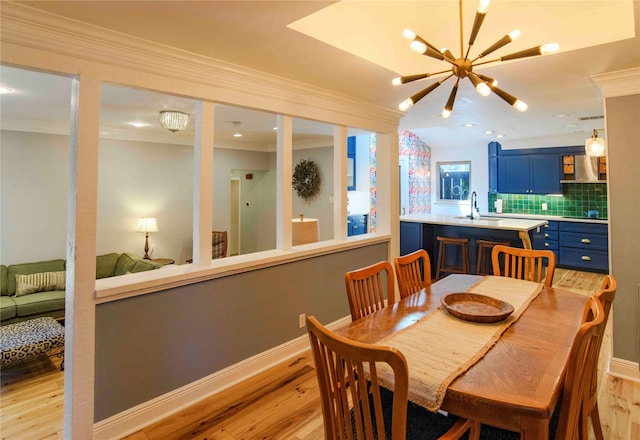 dining room with crown molding, sink, a notable chandelier, and light hardwood / wood-style floors