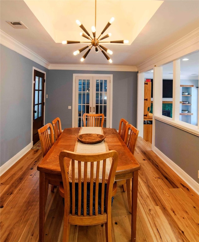 dining area with a notable chandelier, french doors, ornamental molding, and light hardwood / wood-style floors