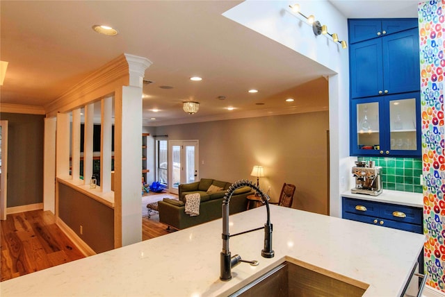 kitchen featuring tasteful backsplash, blue cabinets, ornamental molding, dark wood-type flooring, and light stone counters