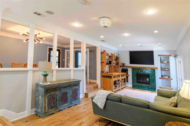 living room with light hardwood / wood-style floors, a fireplace, built in shelves, an inviting chandelier, and ornamental molding