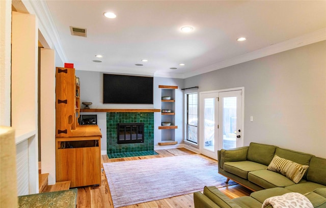 living room featuring built in features, a tile fireplace, light hardwood / wood-style floors, and crown molding