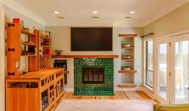 living room with crown molding, a tiled fireplace, and light wood-type flooring