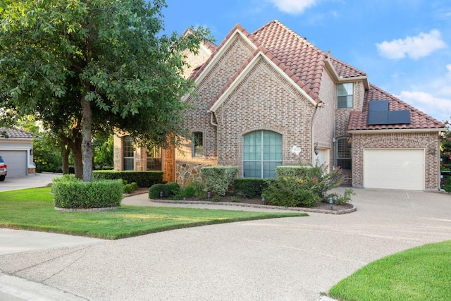 view of front of home featuring driveway, roof mounted solar panels, a tile roof, brick siding, and a garage