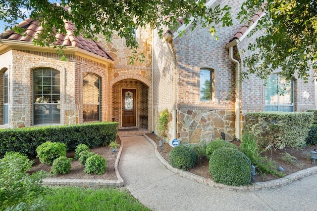 view of exterior entry with brick siding, a tile roof, and stone siding