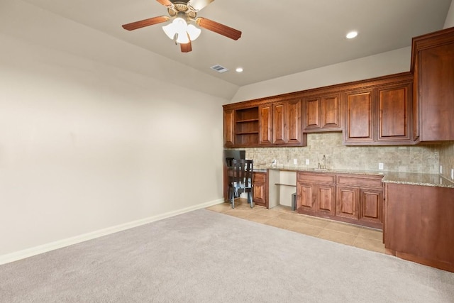 kitchen featuring vaulted ceiling, tasteful backsplash, light colored carpet, ceiling fan, and light stone counters