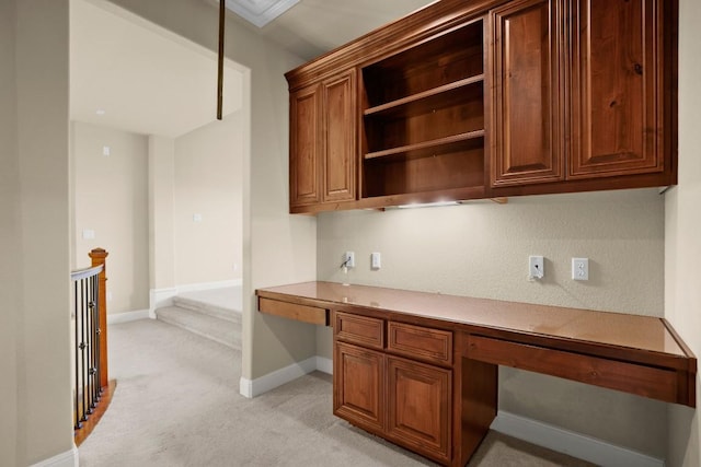 unfurnished office with baseboards, built in desk, and light carpet