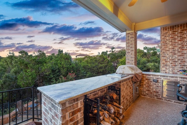 patio terrace at dusk with ceiling fan, a bar, and an outdoor kitchen