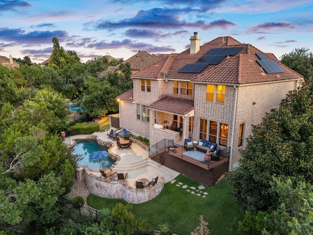 back of house at dusk with an outdoor living space with a fire pit, a chimney, outdoor dining space, solar panels, and a fenced backyard