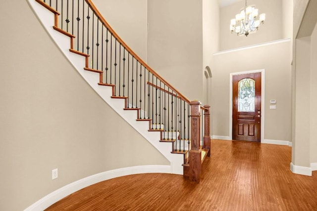 foyer featuring stairway, baseboards, an inviting chandelier, a towering ceiling, and wood finished floors