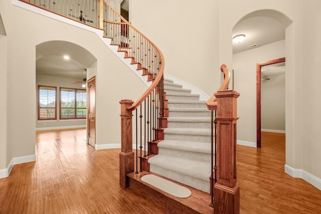 staircase featuring ceiling fan, visible vents, baseboards, arched walkways, and wood finished floors