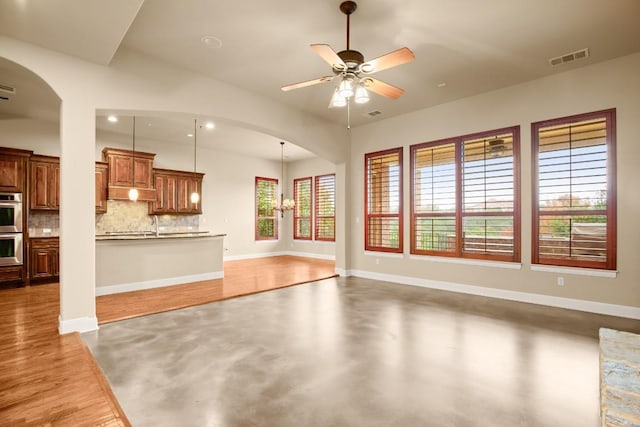 unfurnished living room featuring concrete floors and ceiling fan with notable chandelier