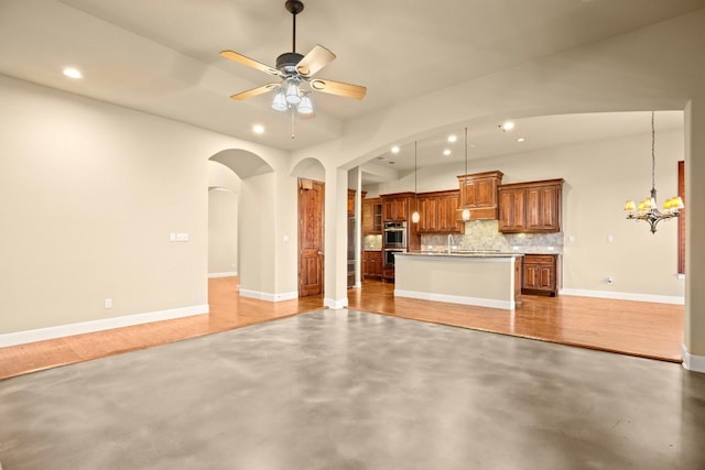 kitchen featuring pendant lighting, backsplash, ceiling fan with notable chandelier, a center island, and stainless steel double oven