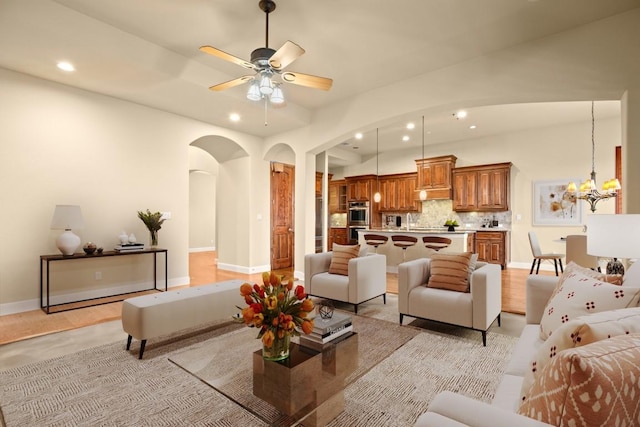 living room featuring baseboards, recessed lighting, arched walkways, and ceiling fan with notable chandelier