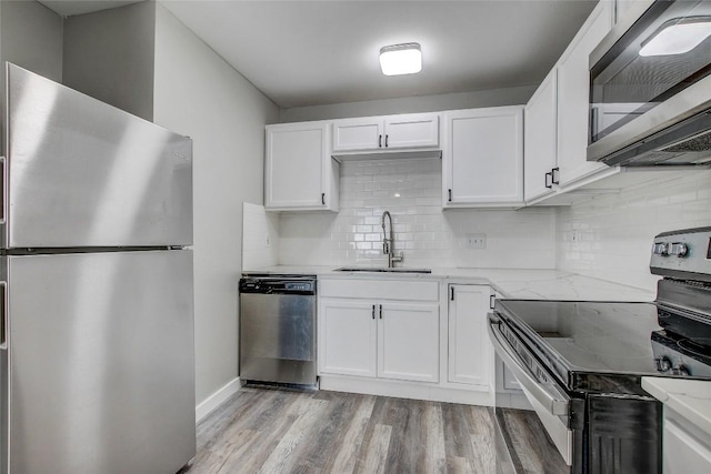 kitchen with appliances with stainless steel finishes, sink, white cabinets, light stone counters, and light wood-type flooring