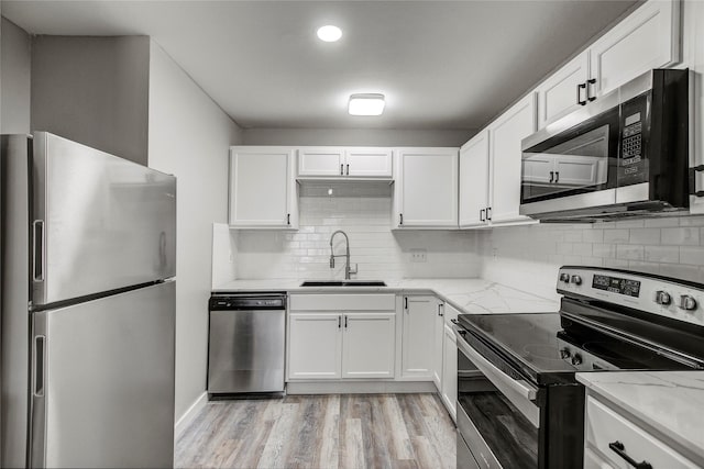 kitchen featuring appliances with stainless steel finishes, white cabinetry, sink, light stone countertops, and light wood-type flooring