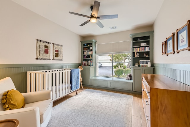 bedroom featuring ceiling fan, light wood-type flooring, and a crib