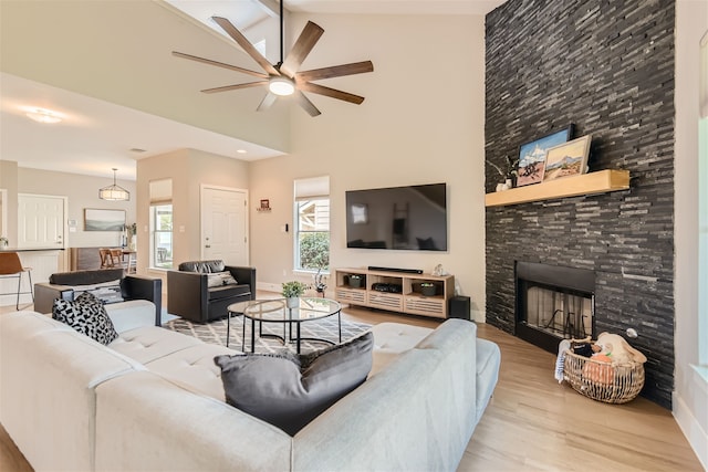 living room with ceiling fan, light hardwood / wood-style flooring, high vaulted ceiling, and a stone fireplace