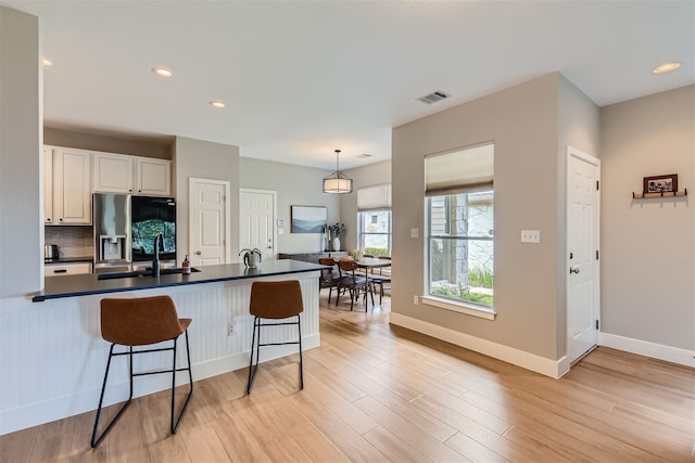 kitchen featuring white cabinets, light hardwood / wood-style floors, hanging light fixtures, stainless steel fridge, and a breakfast bar area