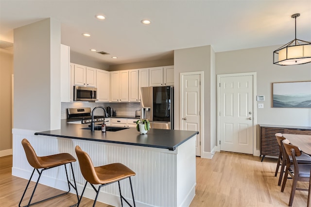 kitchen with a kitchen bar, kitchen peninsula, stainless steel appliances, pendant lighting, and white cabinets