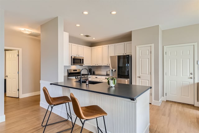 kitchen with kitchen peninsula, sink, white cabinetry, appliances with stainless steel finishes, and a breakfast bar area