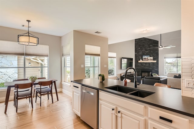 kitchen with decorative light fixtures, dishwasher, sink, light wood-type flooring, and a stone fireplace