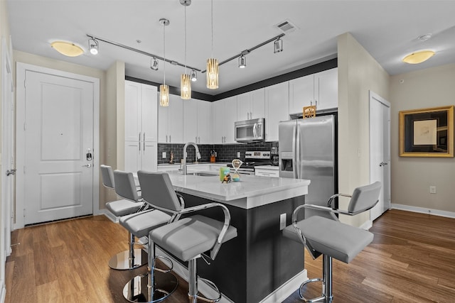 kitchen with appliances with stainless steel finishes, tasteful backsplash, track lighting, hardwood / wood-style floors, and white cabinetry