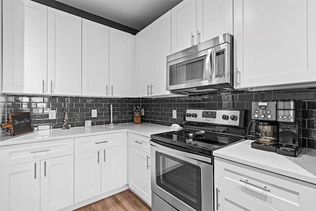 kitchen with stainless steel appliances, white cabinets, decorative backsplash, light wood-type flooring, and light stone counters