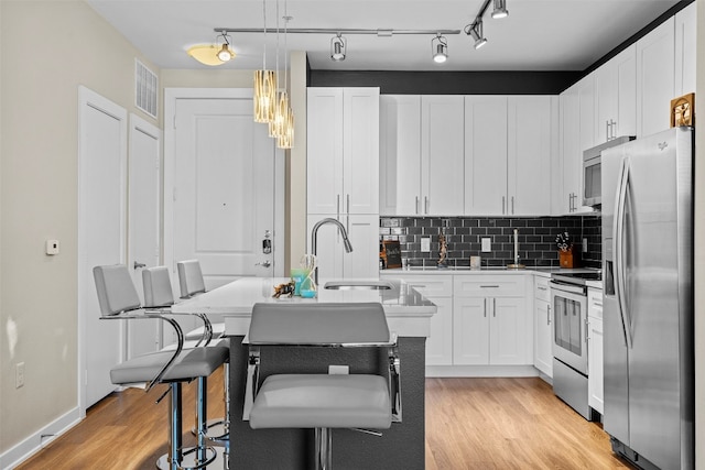 kitchen featuring light wood-type flooring, appliances with stainless steel finishes, sink, pendant lighting, and a center island with sink