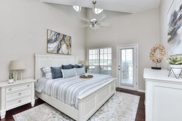 bedroom featuring ceiling fan, dark hardwood / wood-style flooring, access to exterior, and a high ceiling