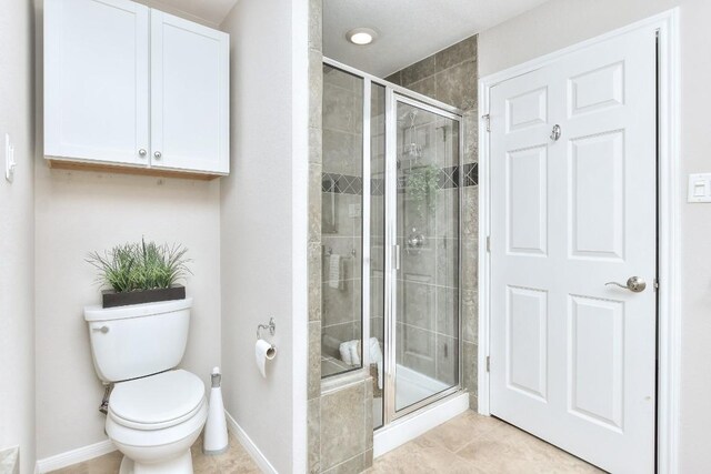 bathroom with tile patterned floors, toilet, and a shower with shower door