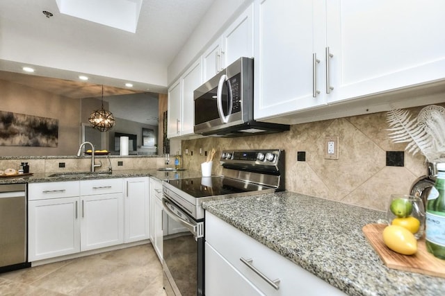 kitchen with appliances with stainless steel finishes, tasteful backsplash, white cabinetry, sink, and hanging light fixtures