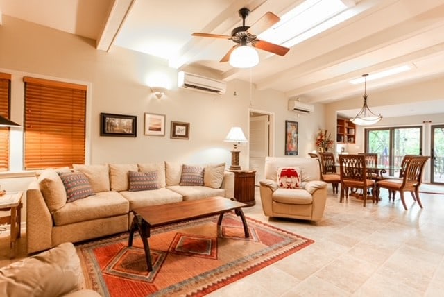 tiled living room featuring a wall mounted air conditioner, beamed ceiling, and ceiling fan