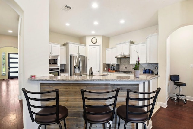 kitchen with white cabinets, dark hardwood / wood-style flooring, stainless steel appliances, backsplash, and kitchen peninsula