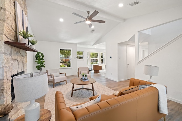 living room featuring vaulted ceiling with beams, a stone fireplace, hardwood / wood-style flooring, and ceiling fan