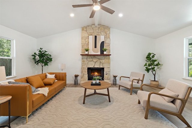 living room with light hardwood / wood-style floors, vaulted ceiling with beams, a stone fireplace, and ceiling fan