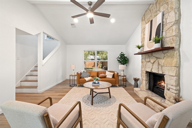 living room with light hardwood / wood-style floors, a stone fireplace, vaulted ceiling, and ceiling fan