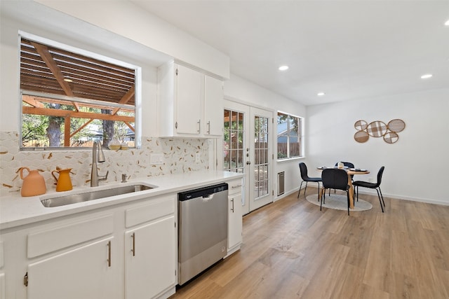 kitchen featuring decorative backsplash, light hardwood / wood-style floors, white cabinets, dishwasher, and sink