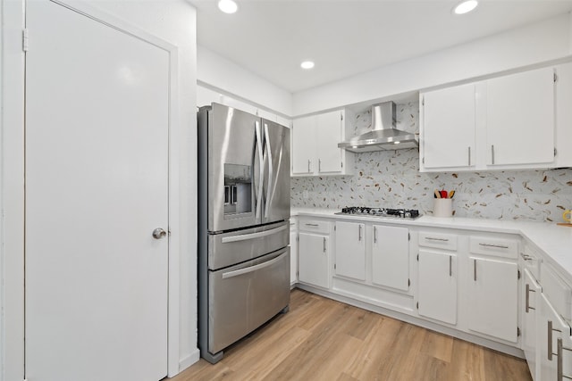 kitchen with white cabinets, tasteful backsplash, wall chimney exhaust hood, light hardwood / wood-style flooring, and appliances with stainless steel finishes