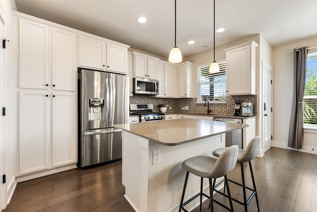 kitchen featuring sink, hanging light fixtures, stainless steel appliances, white cabinets, and a kitchen island