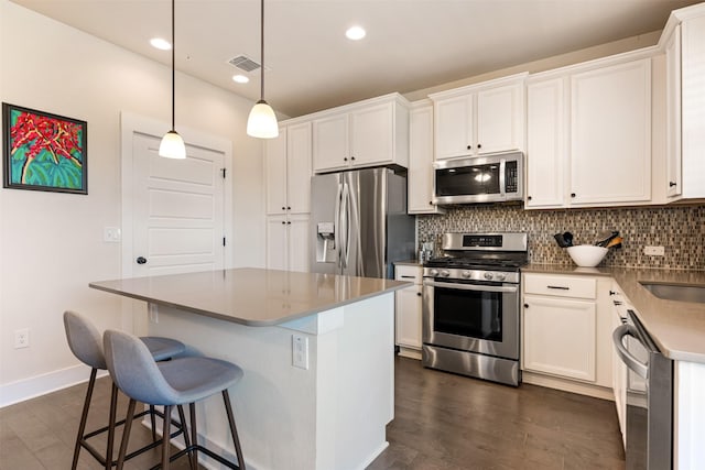 kitchen with white cabinetry, appliances with stainless steel finishes, decorative light fixtures, and a kitchen island