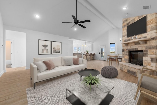 living room featuring beamed ceiling, ceiling fan, a stone fireplace, and light wood-type flooring