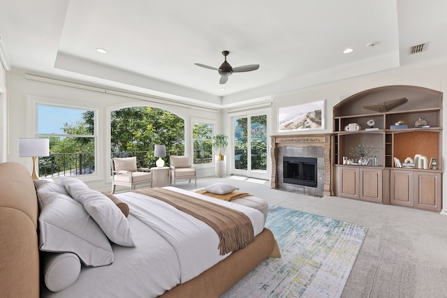 bedroom with a tiled fireplace, light carpet, ceiling fan, and a raised ceiling