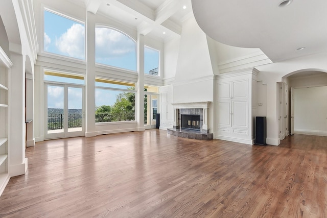 unfurnished living room with beam ceiling, coffered ceiling, a fireplace, and a high ceiling